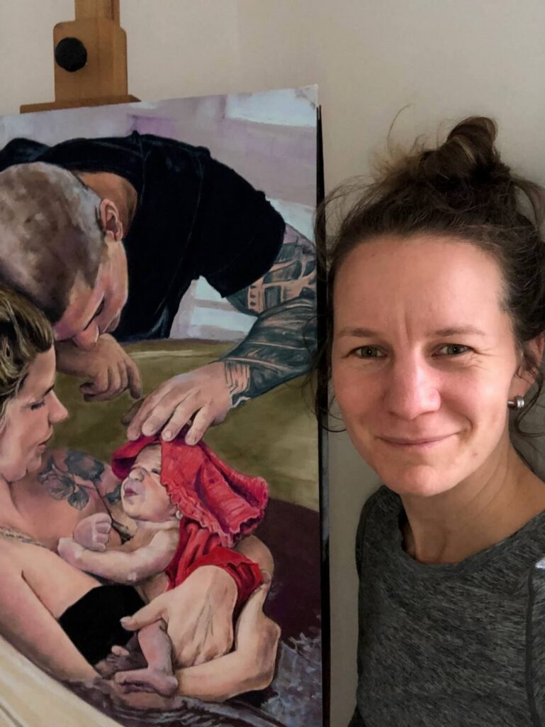 IMG_7870 Pastel artist Monika Zhořová standing next to her painting of a mother, father, and newborn baby.